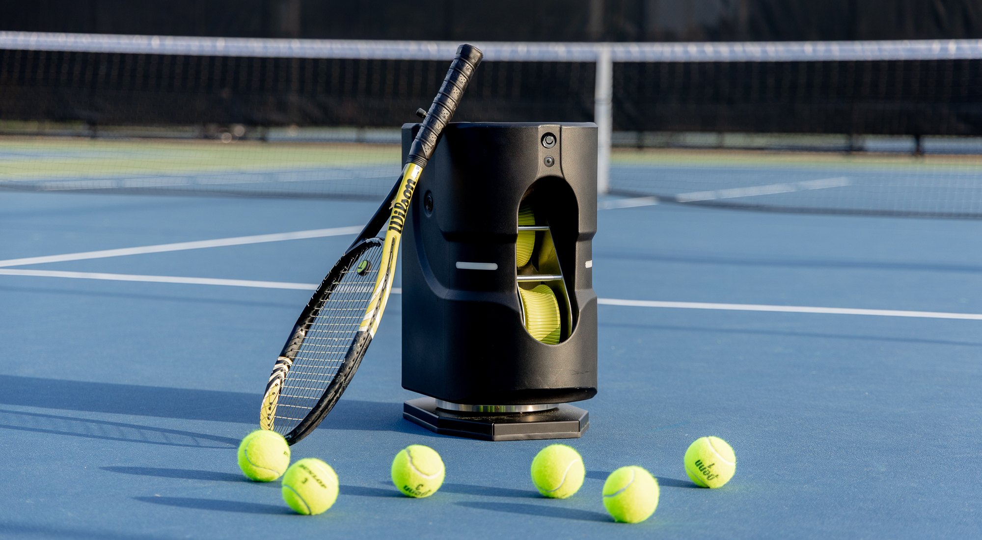 The Tennibot Partner Lite AI ball machine on a tennis court with a racquet leaning against it